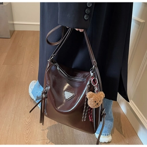 Detail of glossy oil-waxed brown leather tote bag featuring metallic zippers and fringe