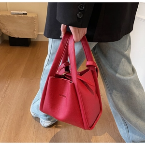 Detail of red pebbled leather bucket bag with top handle and brand logo embossing