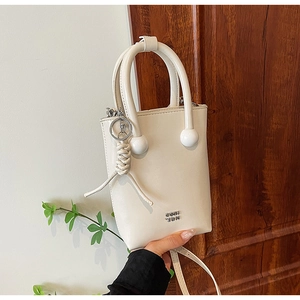 Detailed view of off-white leather phone bag with round handle decor and tassel