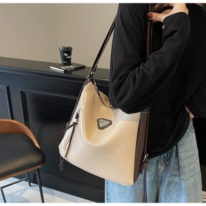 Detail of high-gloss beige and brown tote bag with metal triangle plaque and leather strap