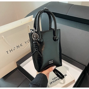 Detailed close-up of glossy black leather handbag with spherical accents and brand lettering