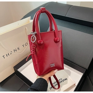 Close-up of a red glossy patent leather handbag with a silver logo in a black gift box