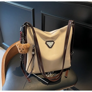 Detail of cream tote bag with brown straps and cute teddy bear charm on dark chair