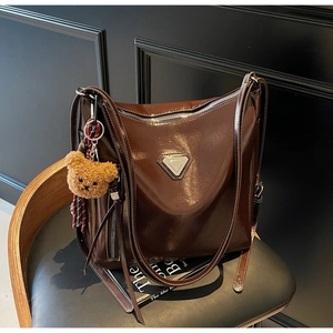 Detail of dark brown glossy tote bag with metal triangle plaque and plush bear charm