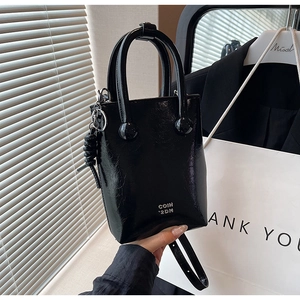 Detail of black glossy handbag featuring pleated texture and metallic logo lettering