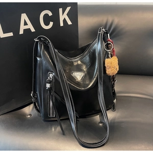 Detail of black glossy leather tote bag featuring side zipper and cute brown bear pendant