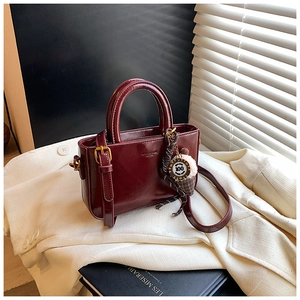 Dettaglio borsa rosso vino in pelle cerata con doppi manici e ciondolo decorativo