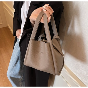 Detailed texture of litchi grain leather bucket bag in elephant gray held by model