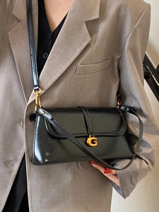 Elegant black patent leather underarm bag with gold metal buckle on a grey suit model