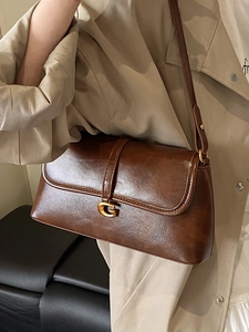 Chic brown leather underarm bag with golden G-buckle worn on a beige trench coat