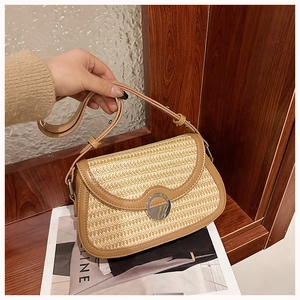 Close-up of woven straw crossbody bag featuring camel leather trim and round metal buckle