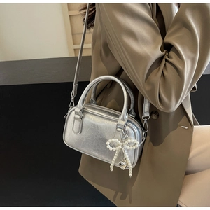 Detail of silver metallic handbag featuring a faux pearl bow charm and heart pendant