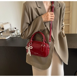 Detail of burgundy glossy leather Boston bag with a pearl bow charm and shoulder strap