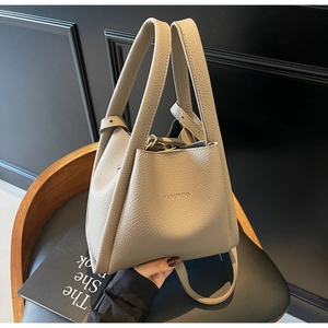 Detail showing litchi grain texture and embossed brand logo on the beige bucket bag