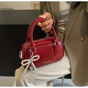 Detail of burgundy oil wax leather Boston bag with pearl bow charm and logo