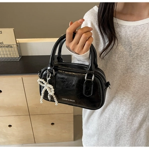 Detail of black glossy mini Boston bag with pearl bow pendant and silver hardware