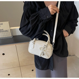 Detail of cream white mini Boston bag with pearl bow charm and silver heart pendant
