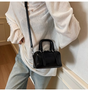 Sac Boston noir brillant avec détails argentés et bandoulière présenté en situation réelle