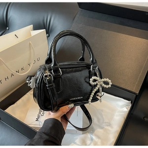 Close-up of black glossy mini Boston bag with pearl bow and heart charm in a luxury gift box