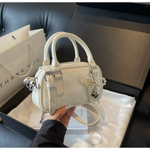 Close-up of a white oil-wax leather Boston bag with a pearl bow and heart charm