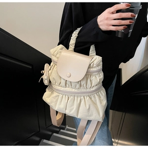 Close-up of beige pleated backpack with mini pouch charm on stylish black stairs