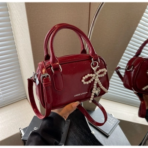 Close-up of red oil wax leather Boston bag with pearl bow and silver heart pendant detail