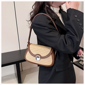 Detail view of woven straw saddle bag with dark brown leather trim and silver metal buckle