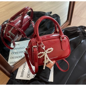 Detail of red wax leather Boston bag featuring a pearl bow charm and logo lettering