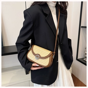 Detail of woven straw crossbody bag with brown leather trim and metal buckle