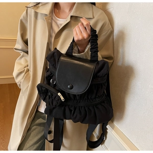 Close-up of black pleated fabric texture and leather flap on trendy fashion backpack
