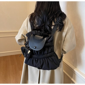 Detail view of black pleated nylon backpack with smooth leather flap and matching mini pouch
