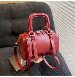 Détail du sac Boston rouge en cuir brillant avec accessoires argentés tenu à la main