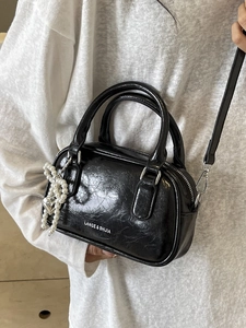 Glossy black oil-waxed leather Boston bag with a pearl heart charm and shoulder strap