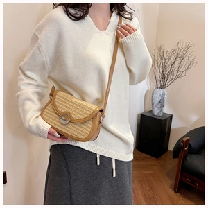 Detail of woven straw shoulder bag with brown leather trim and round metal buckle