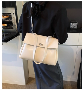Detail view of large cream leather handbag featuring adjustable strap and metal twist lock