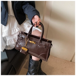 Detail of a dark brown vintage briefcase featuring a gold lock and a mini bag charm