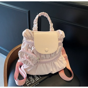 Detail of light pink pleated nylon backpack with a cute bow charm on a dark background