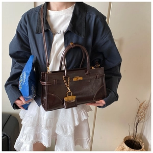 Detailed view of dark brown glossy leather handbag with gold lock and mini bag charm