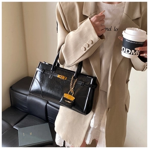 Detail of black pebbled leather tote bag with gold buckle lock and mini coin purse charm