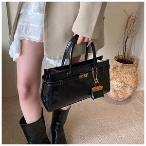 Detail view of a black patent leather satchel featuring a gold lock and mini bag charm