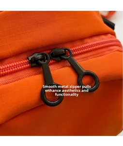 Dettaglio della doppia cerniera in metallo nero su borsa sportiva in tessuto ripstop arancione