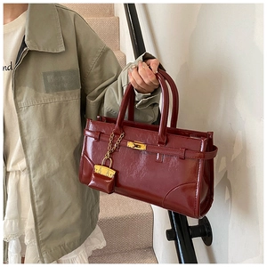Close-up of glossy burgundy leather handbag with golden twist lock and strap detail