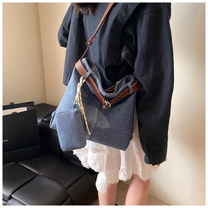 Detail of blue denim tote bag with brown leather straps shown on a model's shoulder