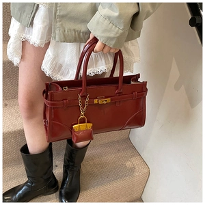 Detail of burgundy leather handbag with golden lock and small hanging charm