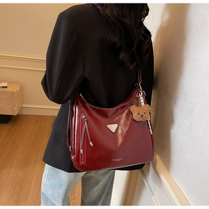 Detailansicht der weinroten Leder-Tote-Bag mit silbernem Dreieckslogo und Teddy-Anhänger