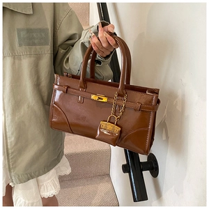 Detail of a deep brown shiny leather handbag with gold buckle and mini purse accessory