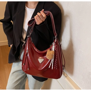 Detailaufnahme der burgunderroten Ölwachs-Ledertasche mit Metall-Logo und Bären-Anhänger
