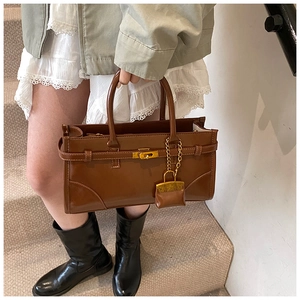 Retro brown leather handbag with gold metal lock and chain charm on stone stairs