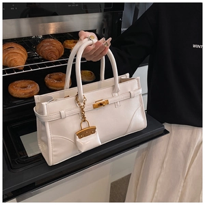 Detail of white leather handbag with golden lock and mini charm in a lifestyle kitchen setting