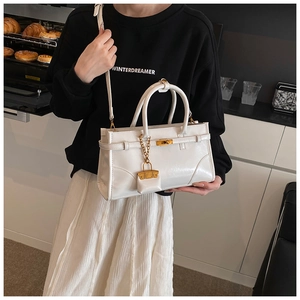 Detail view of a white vintage briefcase style handbag with gold lock and mini charm bag